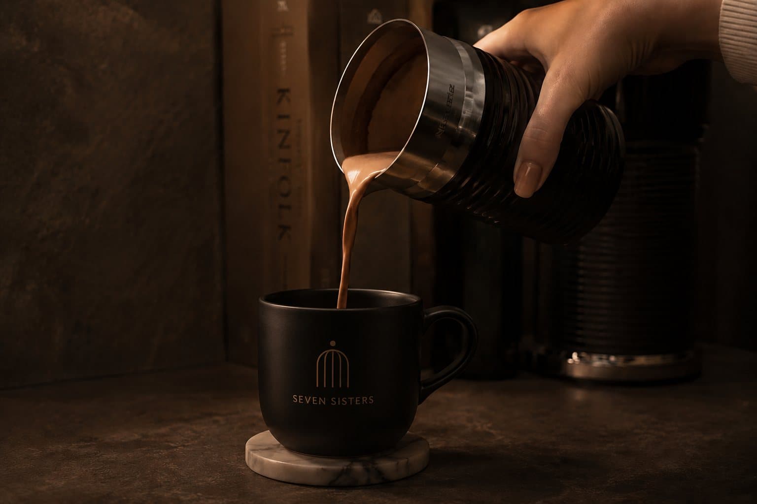 Cacao being poured from a milk frother into a matte black Seven Sisters mug resting on a marble coaster