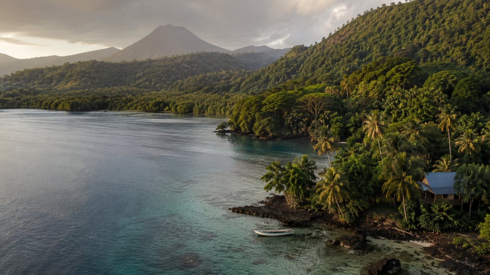 A volcanic peak rising above rainforest and turquoise water in the Solomon Islands, with a small boat moored off a palm-lined shore